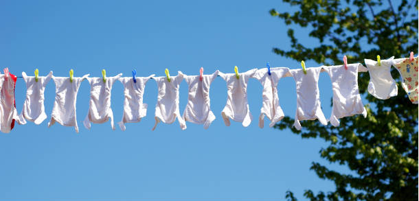 Many cloth nappies on a high washing line with a tree to the right and blue sky in the background