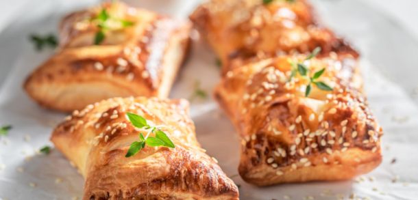 Four golden puff pastry sausage rolls on a tray.