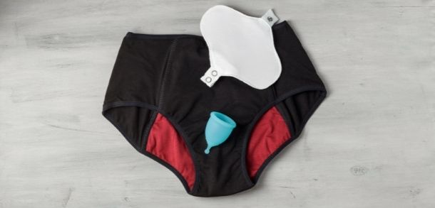 A pair of black and red period pants with a blue menstrual cup and a white reusable sanitary pad.