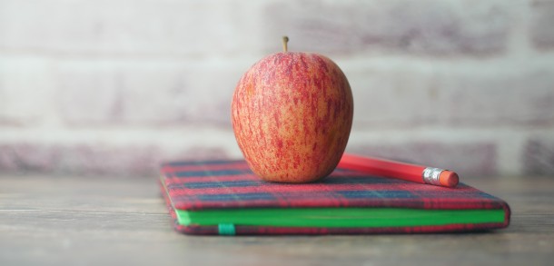 Red apple on top of a notebook with a pencil.