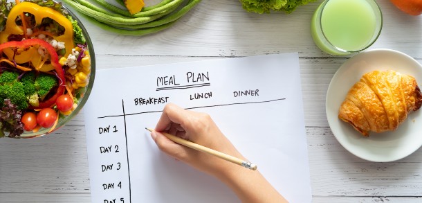 Hand writing out a meal plan on paper surrounded by food.