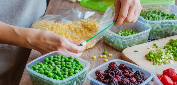 Hands sealing sweetcorn in a freezer bag surrounded by other fresh fruit and vegetables.