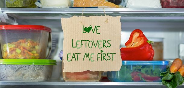 Fridge shelf of plastic containers with leftovers and a sign reading Love leftovers, eat me first.