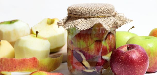 A jar of apple vinegar and some cut and whole apples.