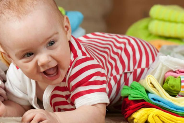 Smiling baby crawling amongst colourful cloth nappies.