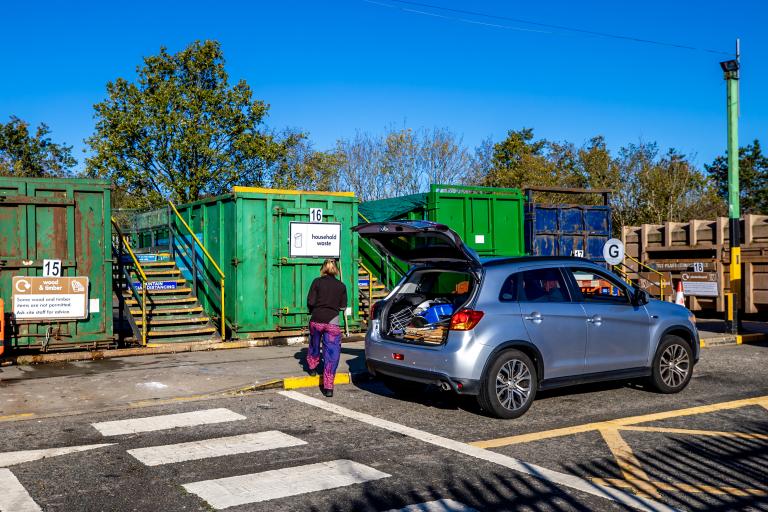 Person next to car with it's boot open at a recycling centre.