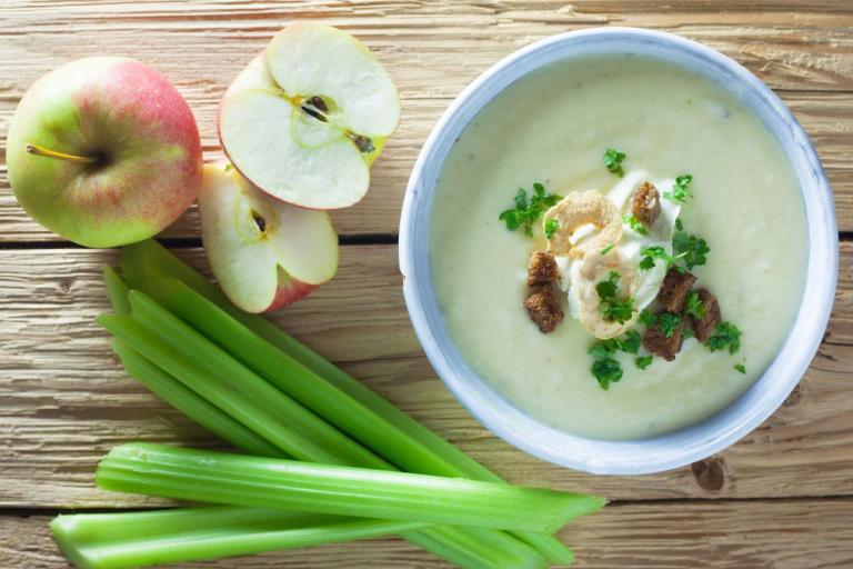 Bowl of soup with apples and celery to the side.