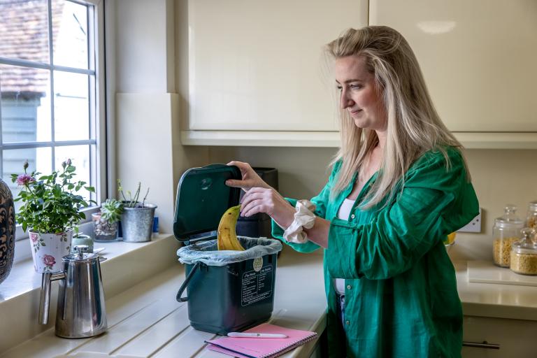 Woman putting banana skin into a food recycling caddy.