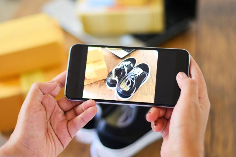 Hands holding a mobile phone taking a picture of a pair of shoes.