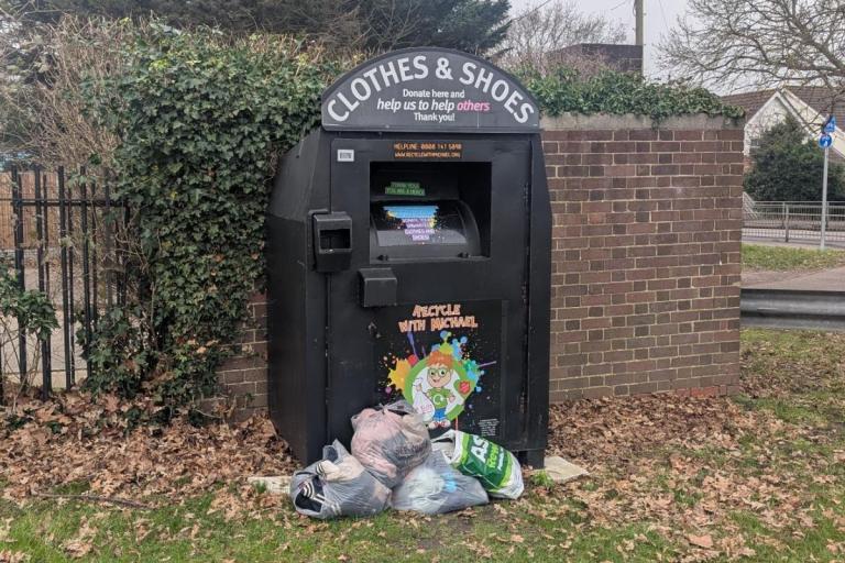 Bags of clothing on the floor in front of a clothing bring bank.