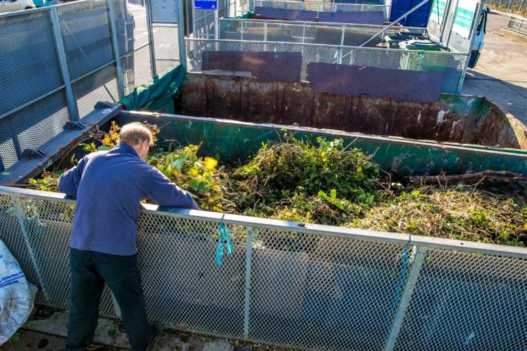 A man putting garden waste in a large container at a recycling centre.