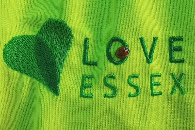 A ladybird resting in the letter O of the Love Essex logo on a yellow hi-vis jacket.
