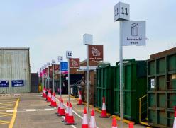 Tall poles have been installed in front of each bin, each with a large sign showing which material goes where. The bins are numbered, and the poles are visible above vehicle height.